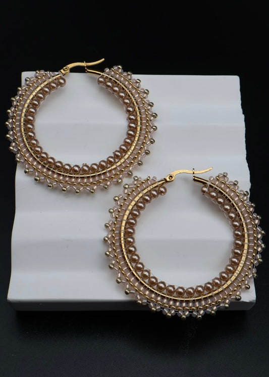 Gold hoop earrings with intricate designs on a white stand against a black background
