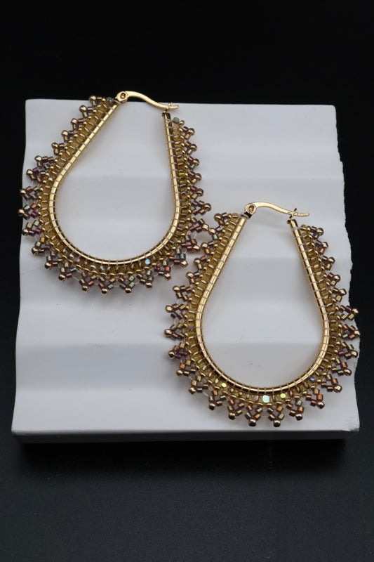 Gold hoop earrings on a white stand with a black background