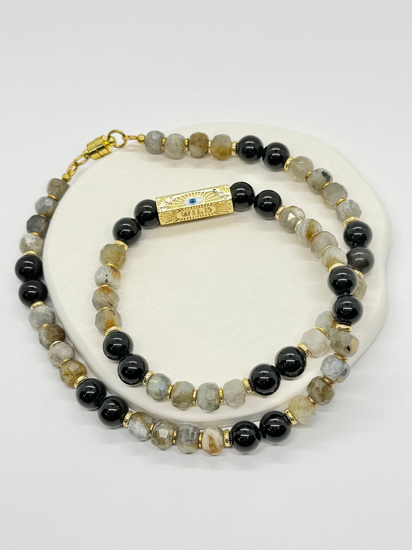 A beaded necklace with black and gray stones on a white surface