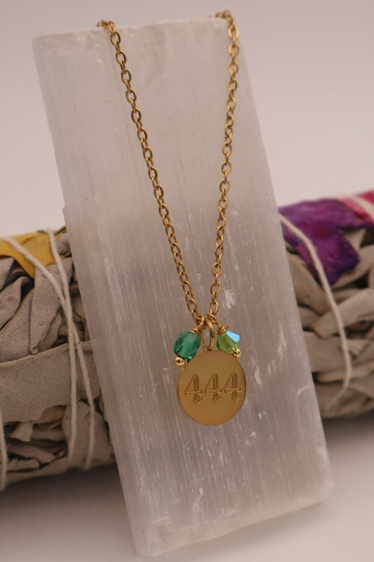 Gold necklace with green beads and a gold pendant on a stone surface