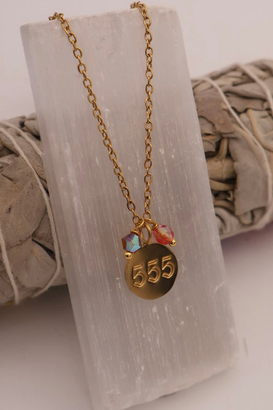 Gold necklace with a '555' pendant on a stone surface