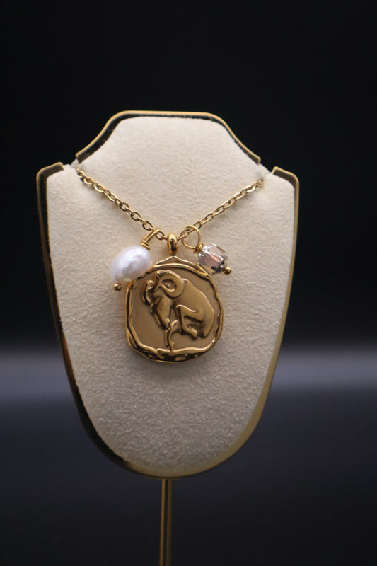 Gold necklace with a pendant on a beige display stand against a dark background