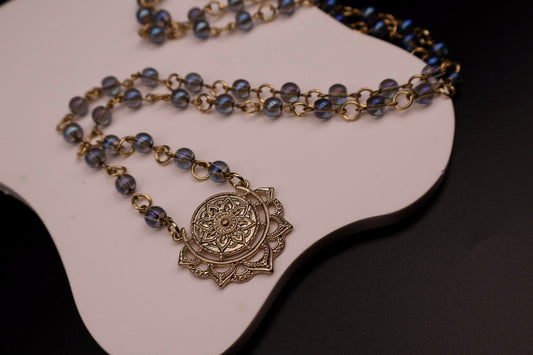 Necklace with blue beads and a decorative pendant on a white stand.