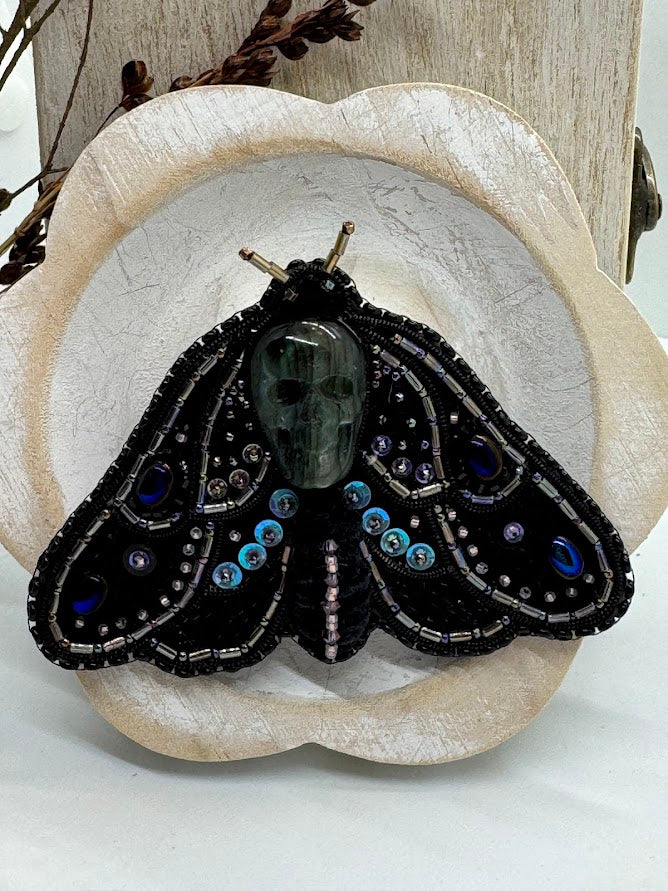 a closeup of a pin of a deaths head hawkmoth pin with a labradorite skull.