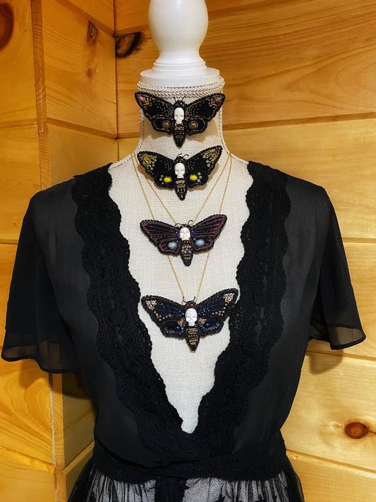 A mannequin with four beaded deaths head hawkmoth pins on it. tow pinned on and two on chains. 