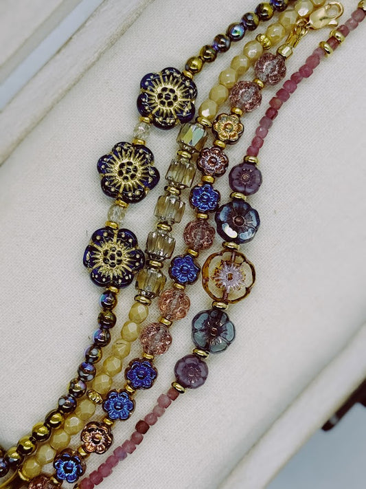 a bracelet with three blue flowers and iridescent beads, bracelet with nude beads and baroque center beads, bracelet with metallic flowers, a bracelet with pink stones and five flowers in the center