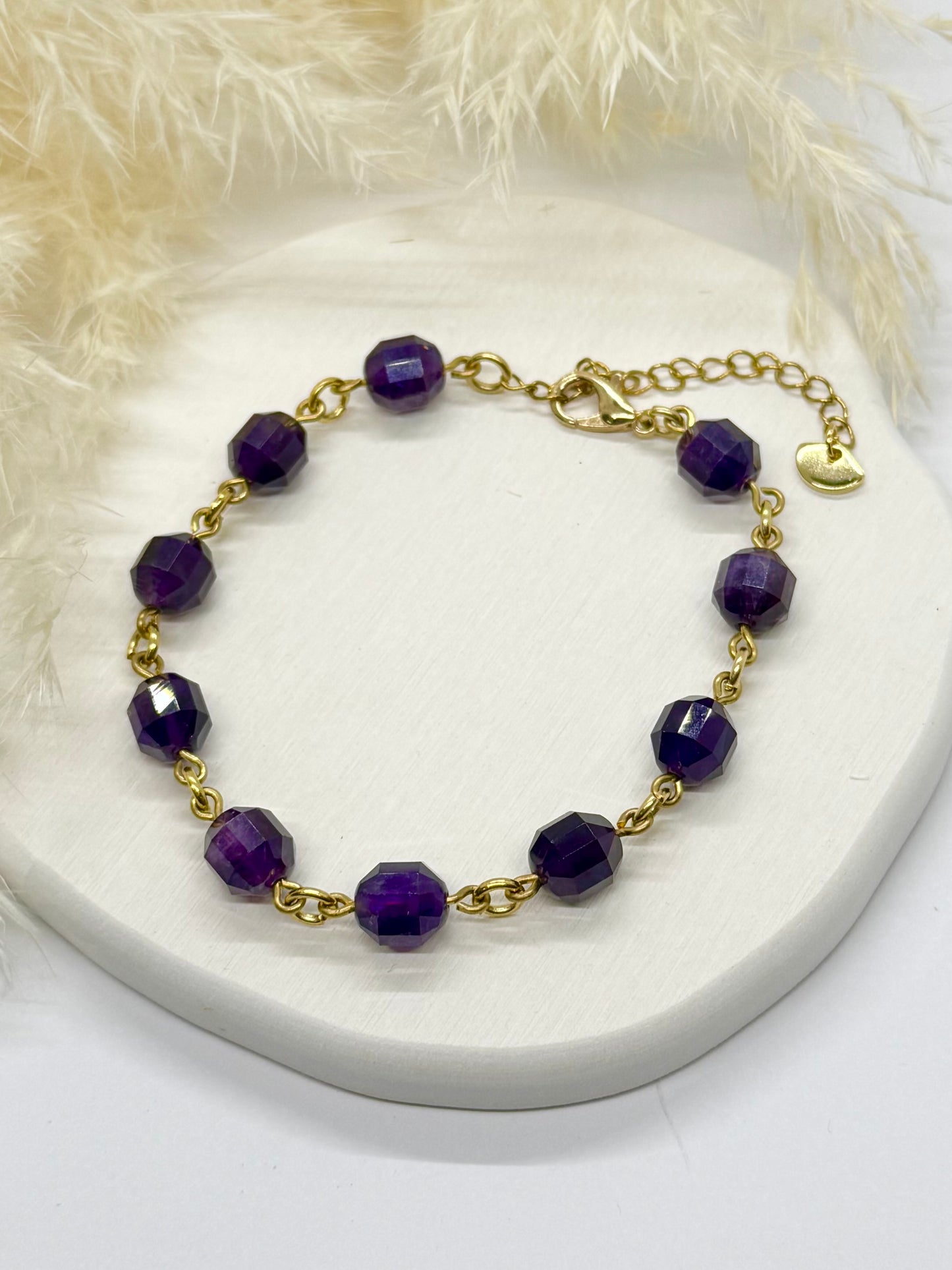 Gold bracelet with purple beads on a white surface
