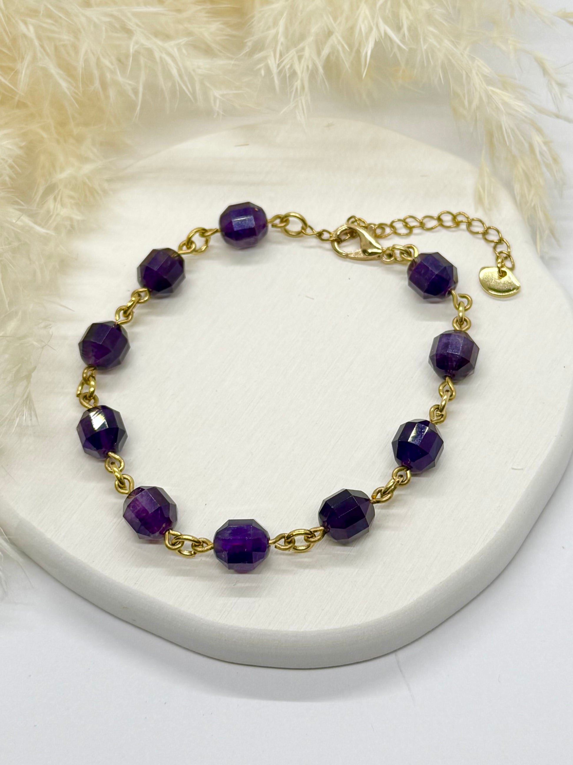 Gold bracelet with purple beads on a white surface