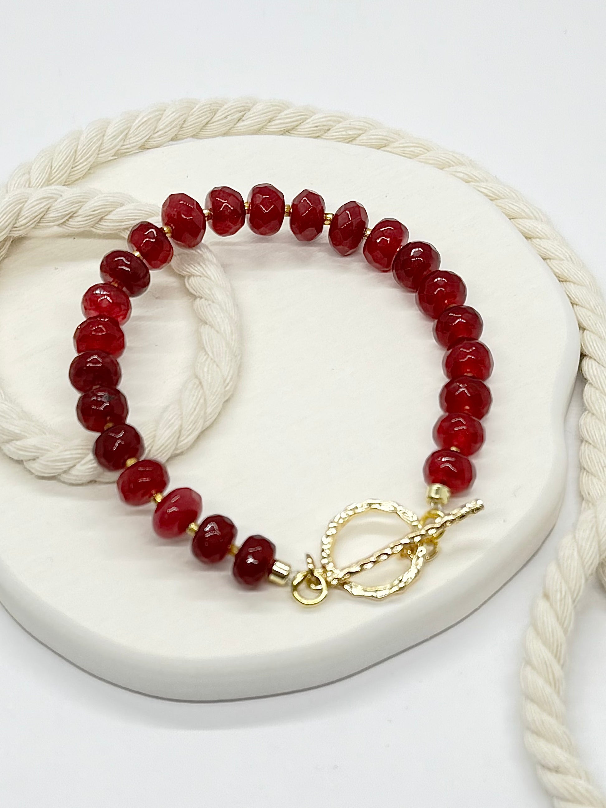 Red beaded bracelet with a gold clasp on a white surface