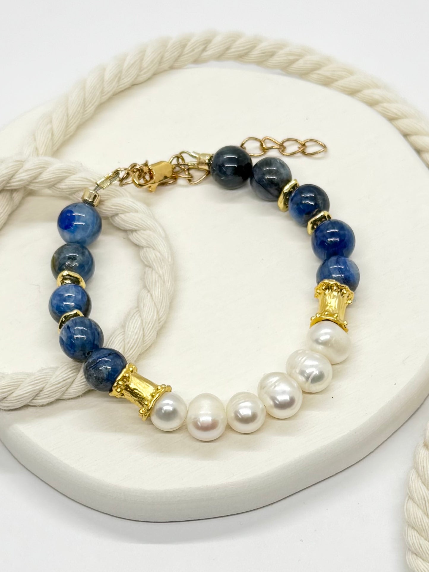 Bracelet with blue beads, gold accents, and pearls on a white rope.