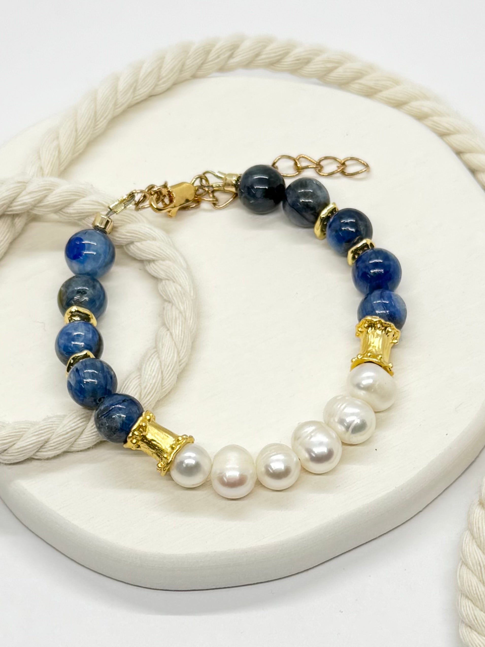 Bracelet with blue beads, gold accents, and pearls on a white rope.
