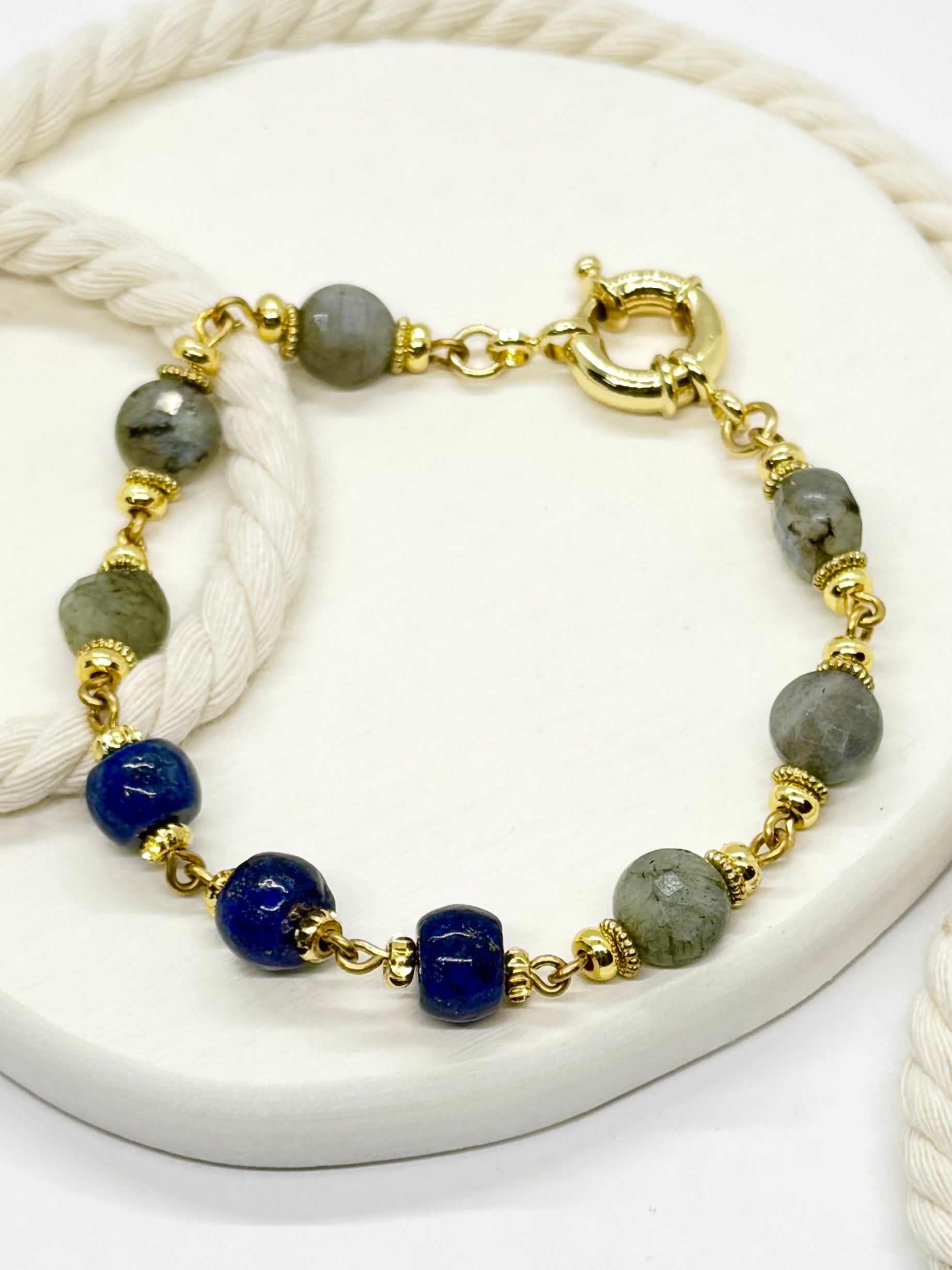 Bracelet with gold chain, blue beads, and gray stones on a white surface