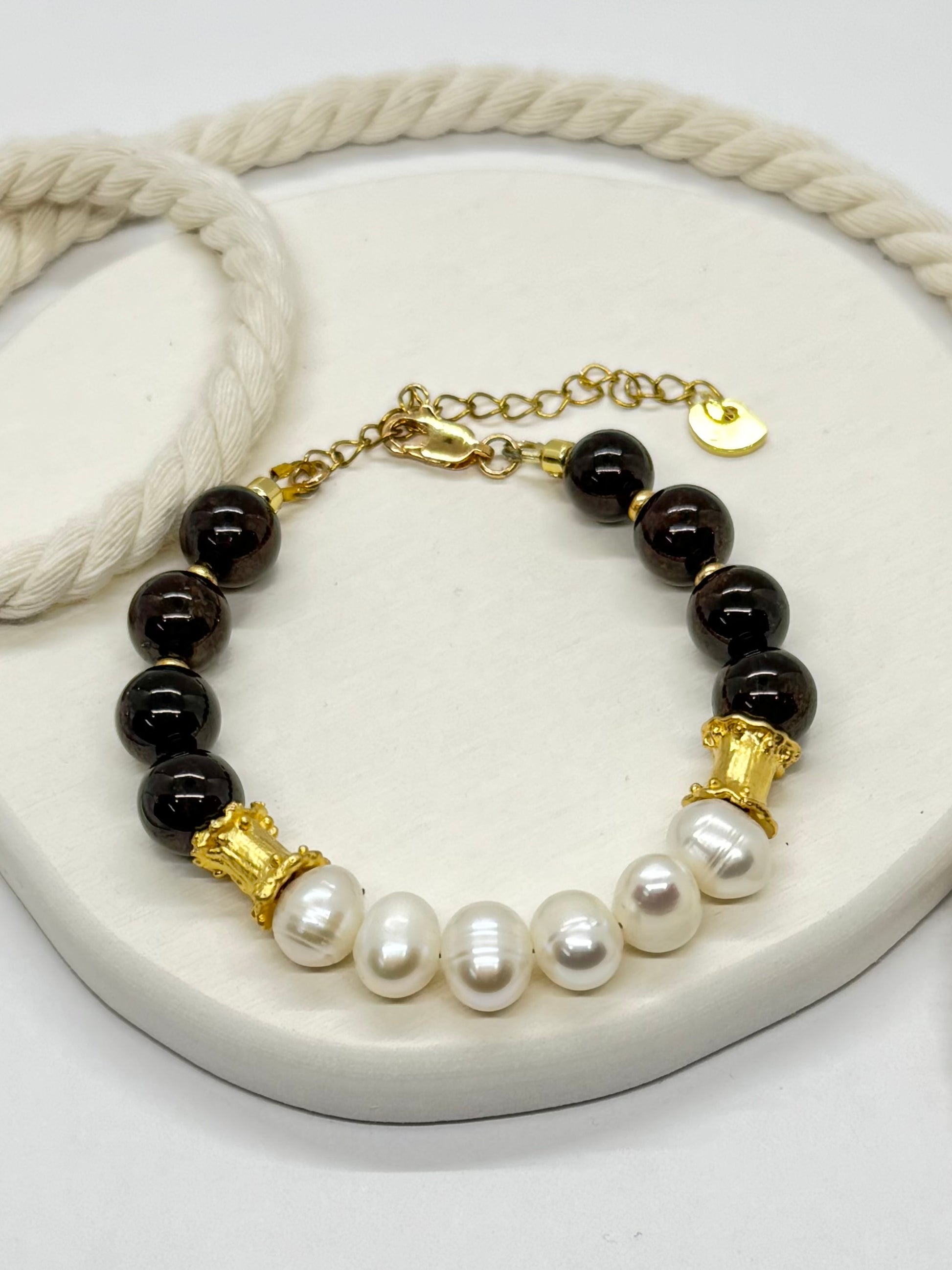 Bracelet with black beads, gold accents, and white pearls on a white surface