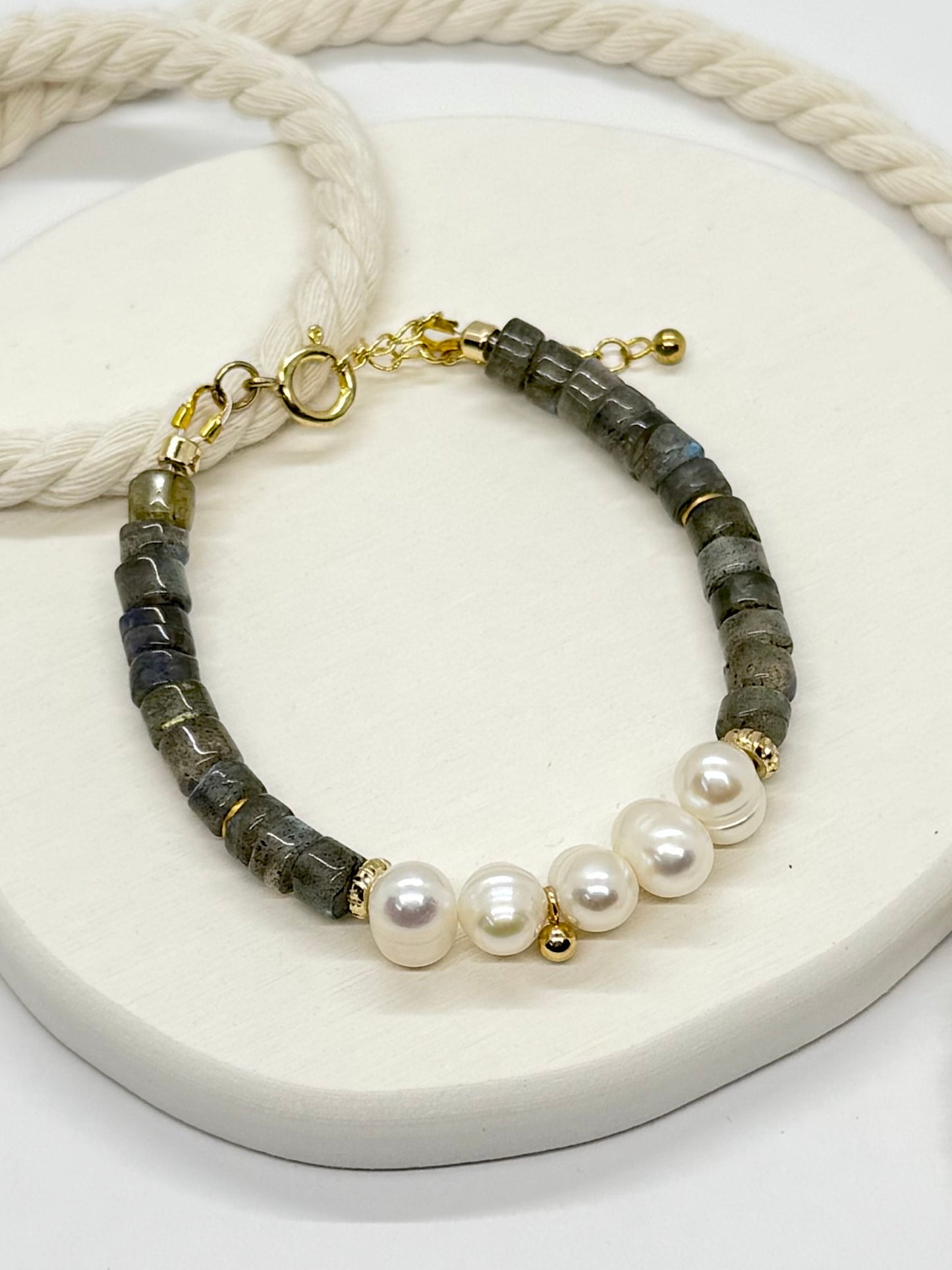 Bracelet with gray beads, pearls, and gold accents on a white surface