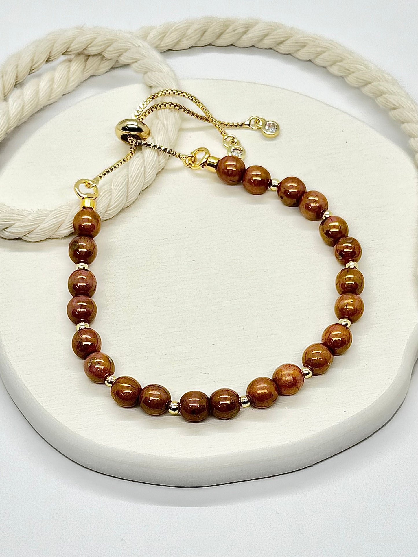 Brown beaded bracelet on a white surface with a beige rope