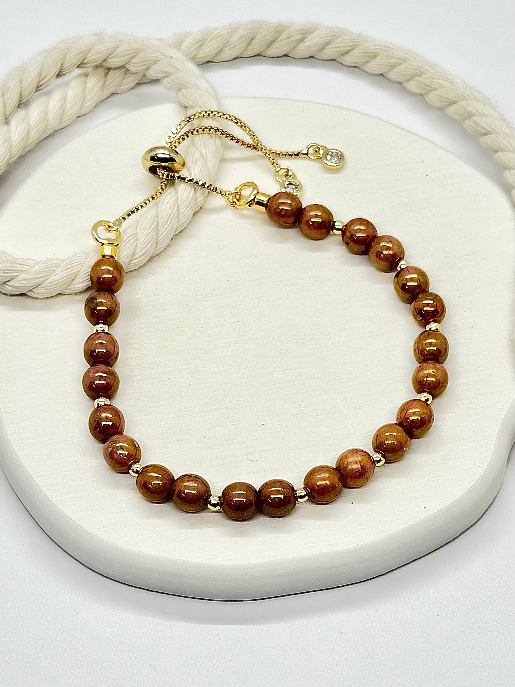 Brown beaded bracelet on a white surface with a beige rope