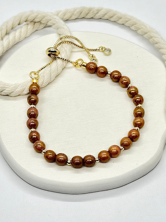 Brown beaded bracelet on a white surface with a beige rope