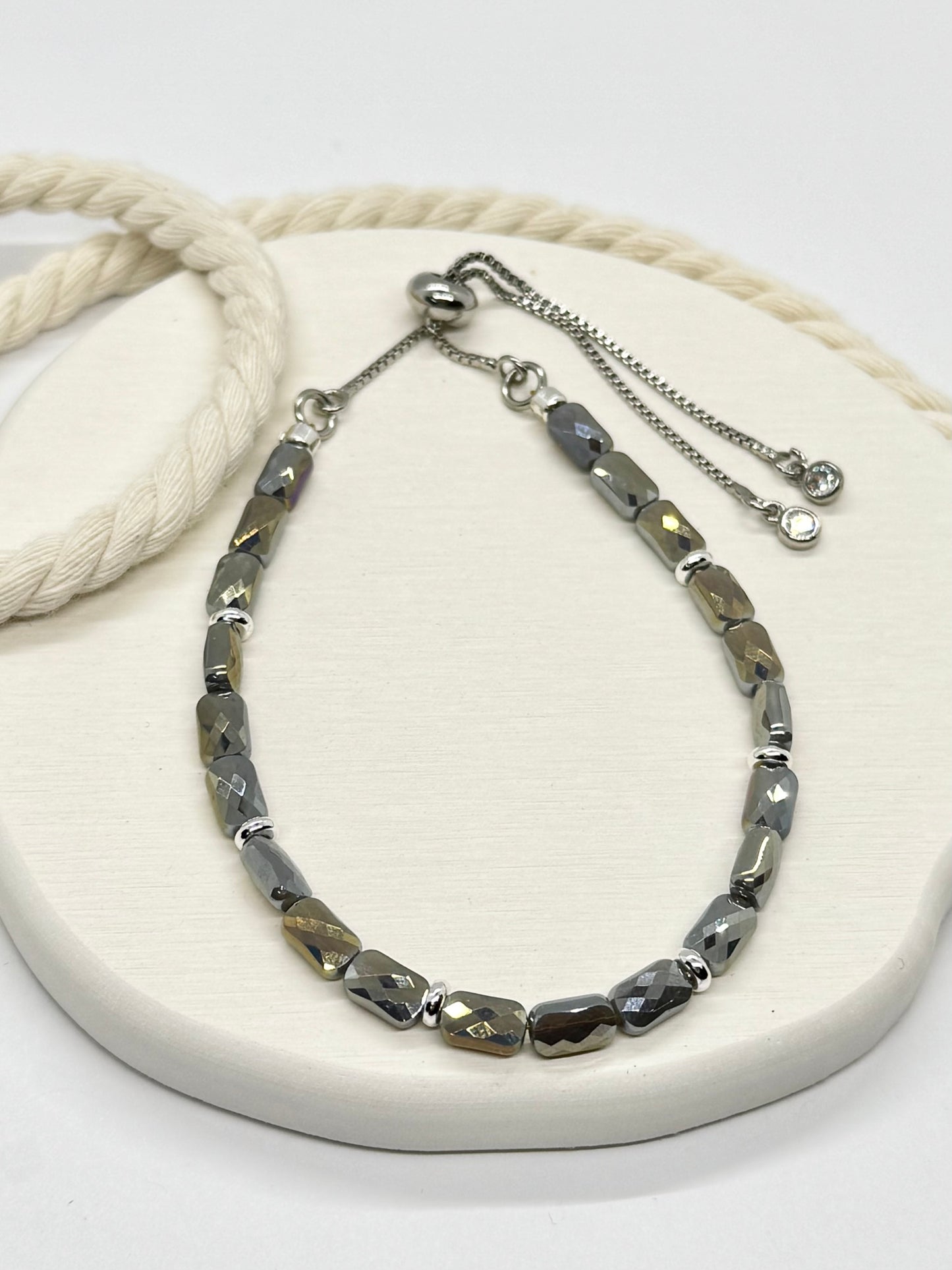 Silver beaded necklace on a white surface with a rope