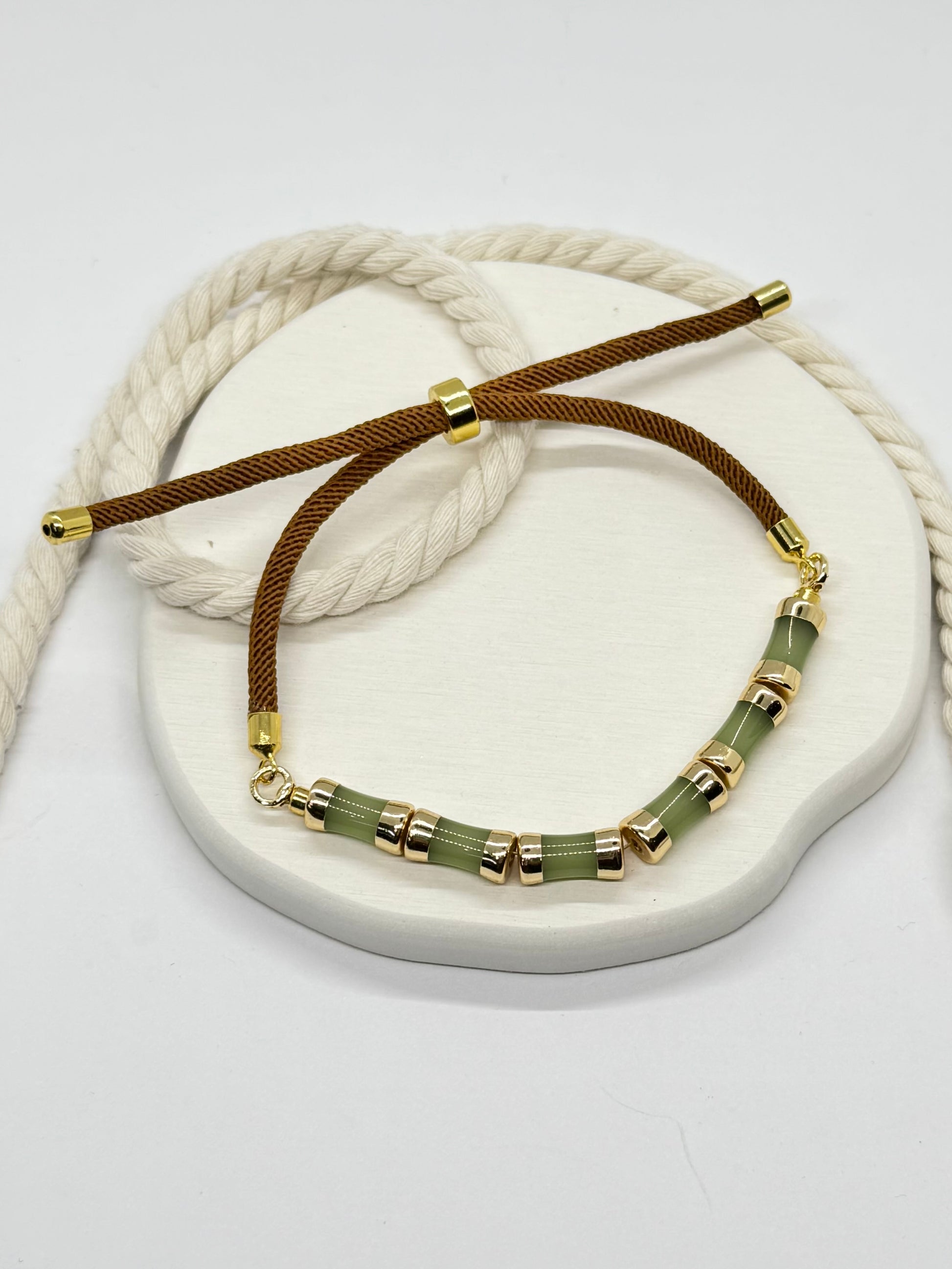 Bracelet with gold beads and brown cord on a white stone surface