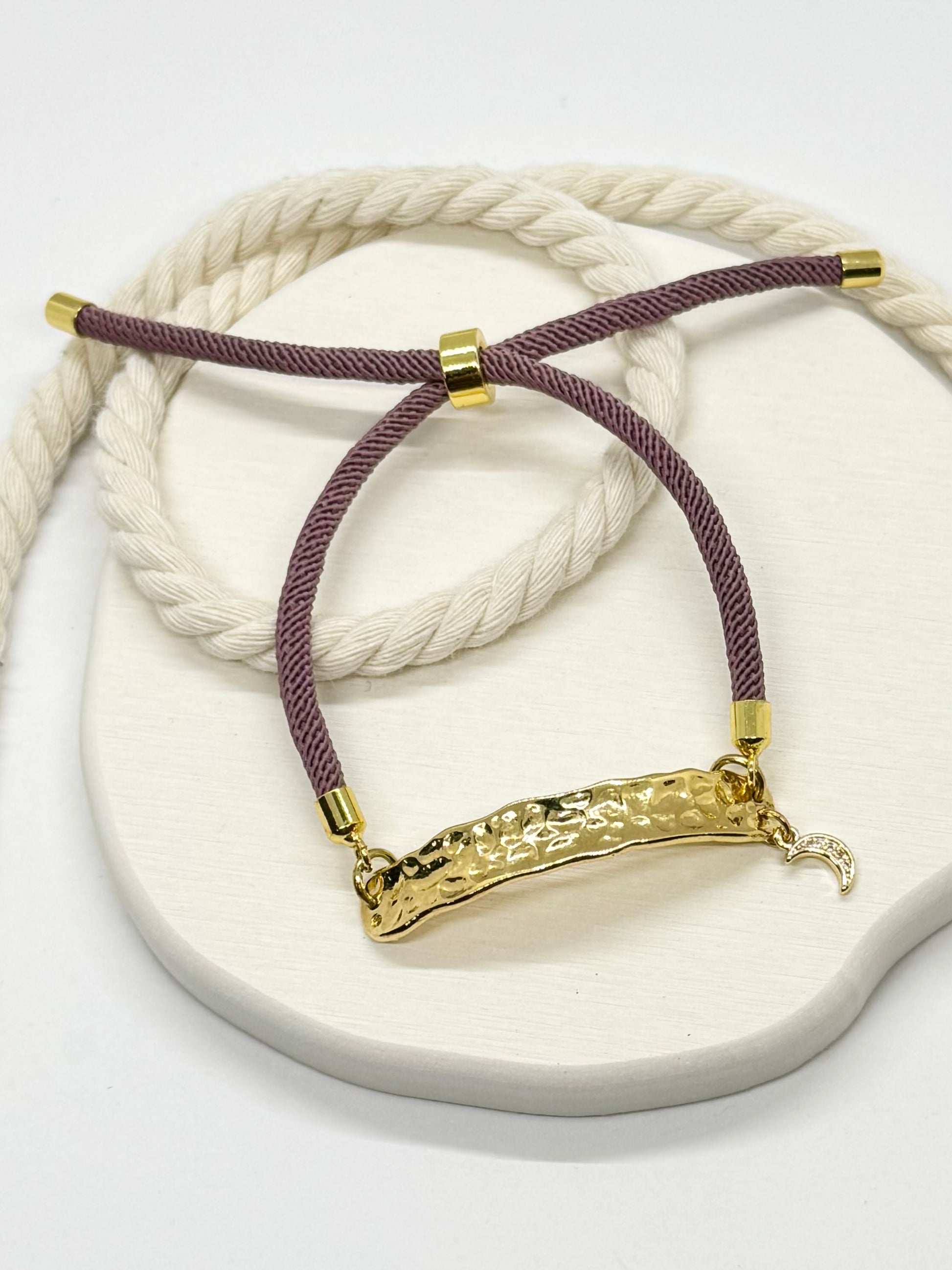 Bracelet with gold clasp and purple cord on a white stone surface