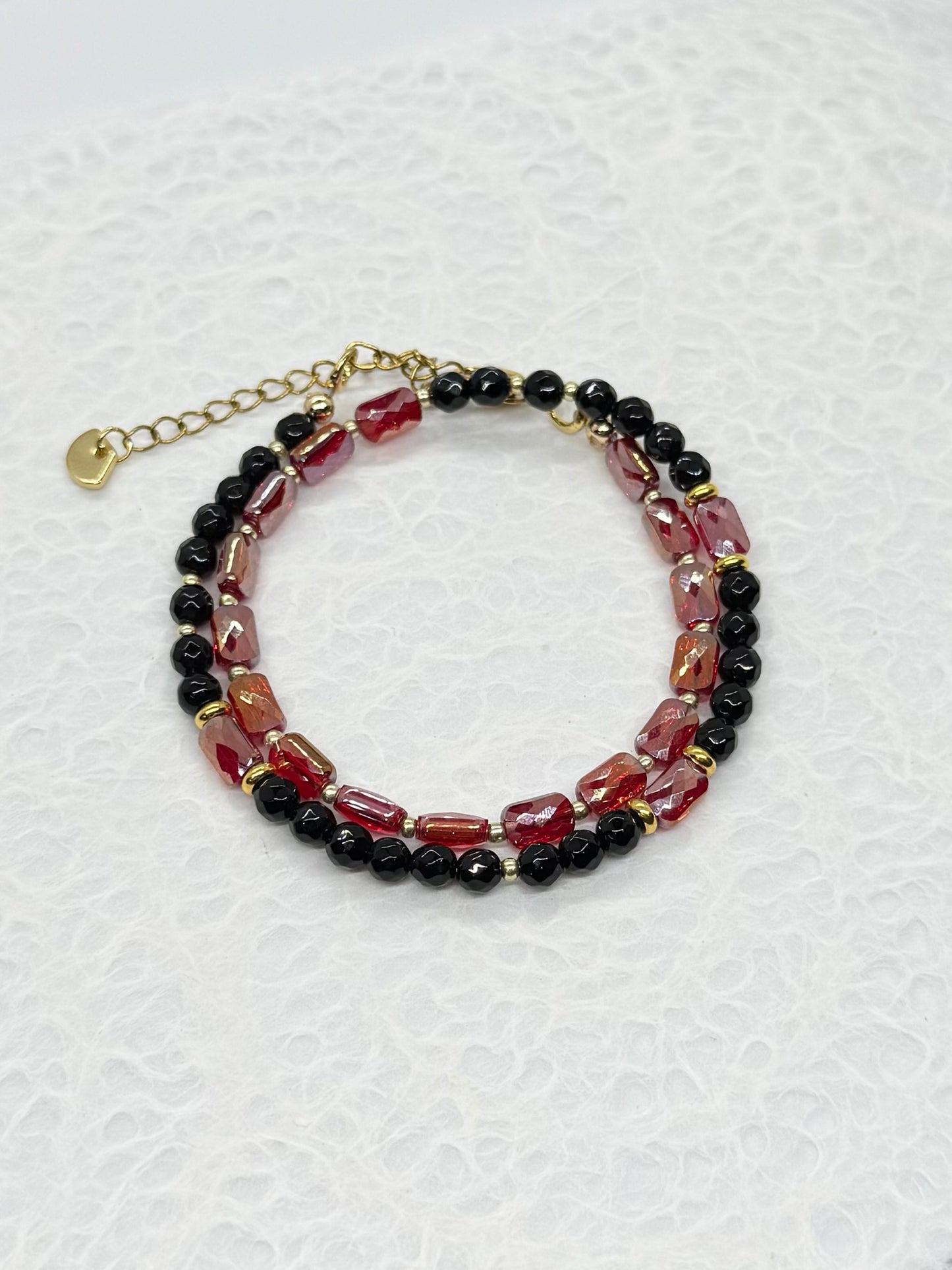 Beaded bracelet with red, black, and gold beads on a white textured background