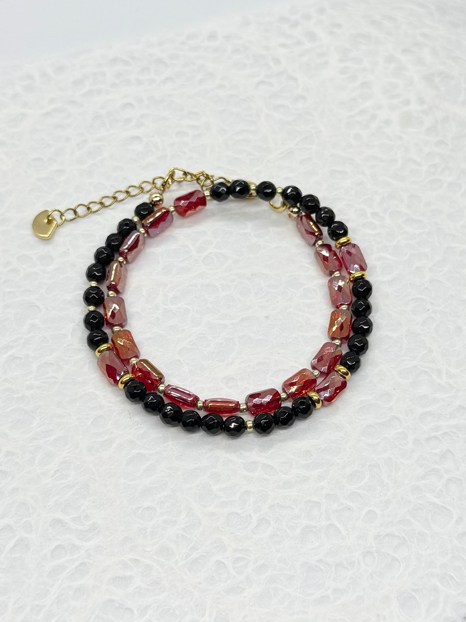Beaded bracelet with red, black, and gold beads on a white textured background