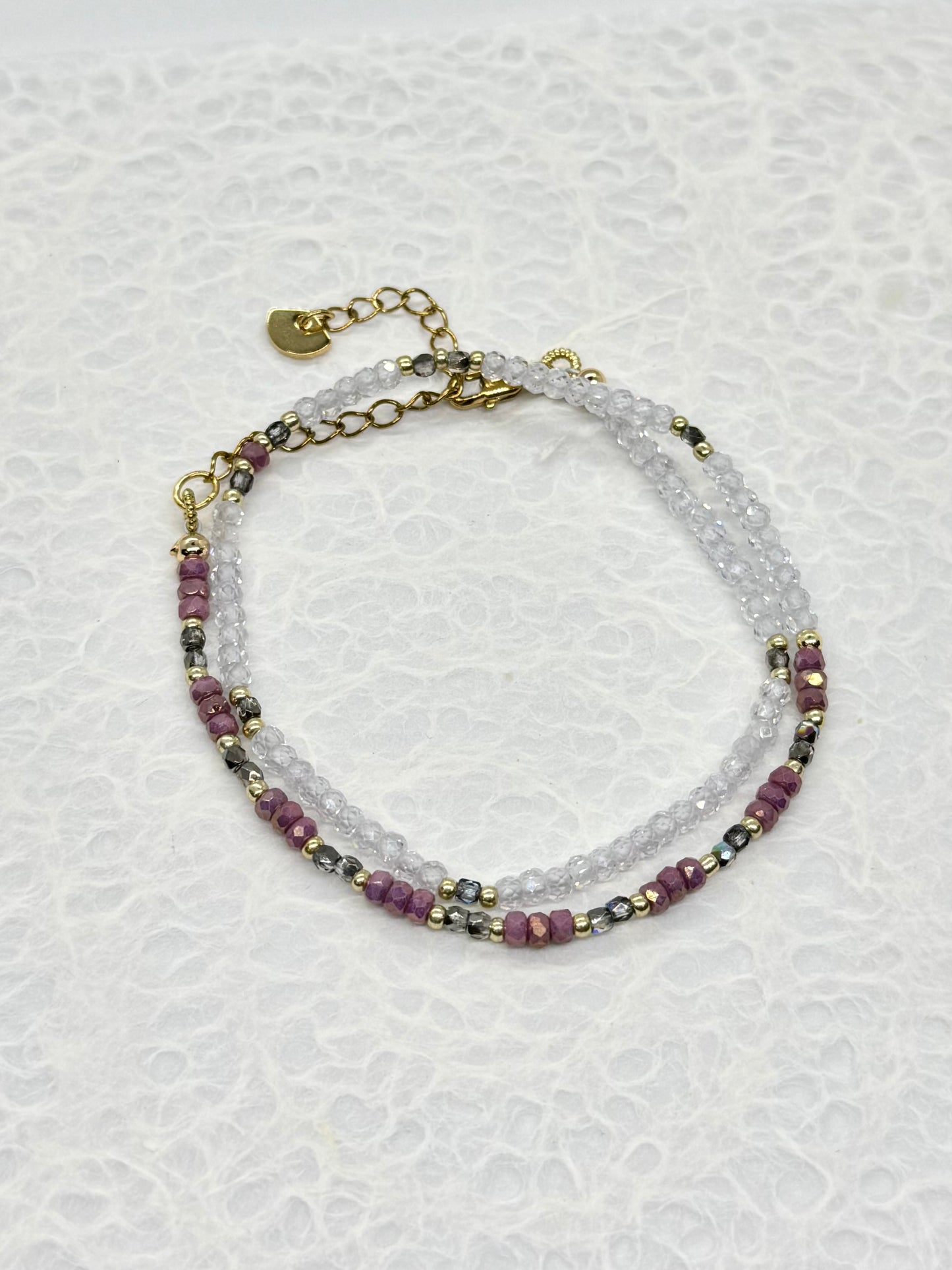 Multistrand beaded bracelet with purple and clear beads on a textured white background