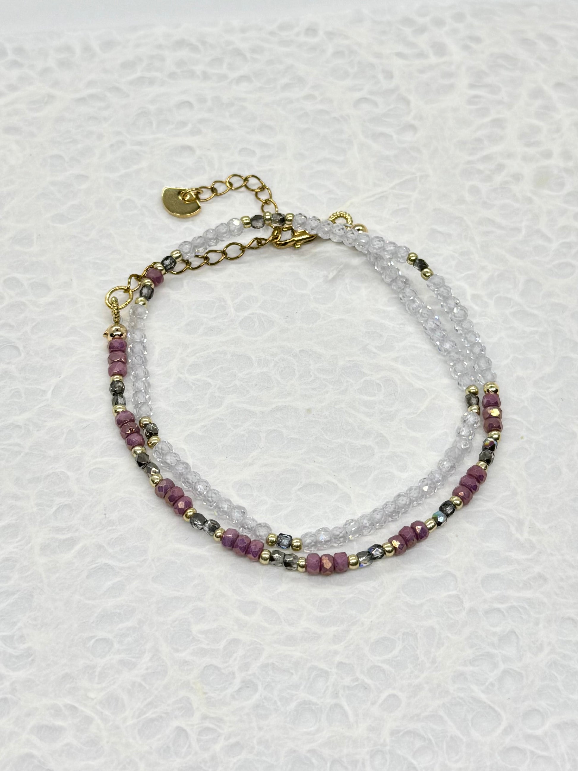 Multistrand beaded bracelet with purple and clear beads on a textured white background