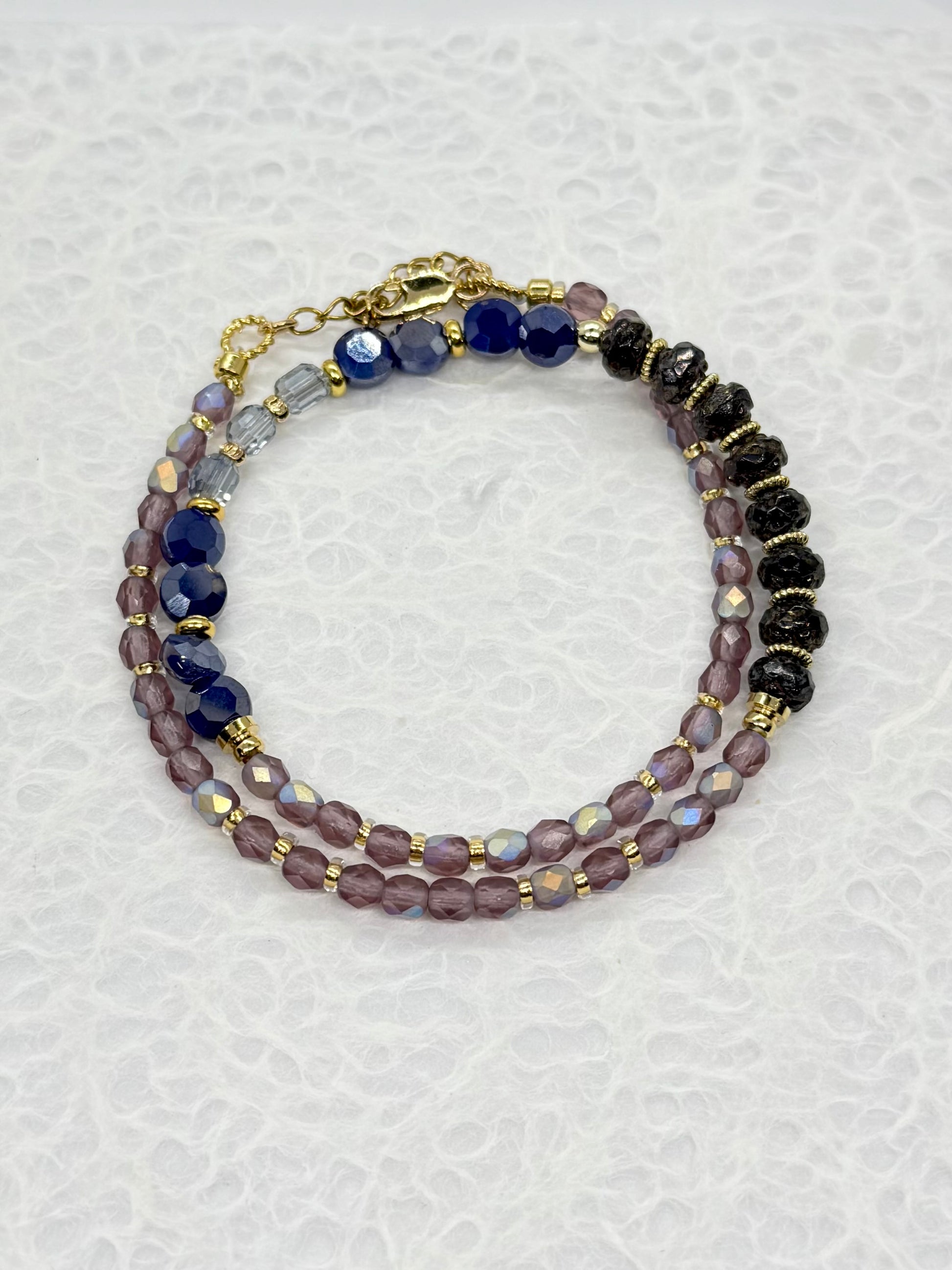 Multistrand beaded bracelet with purple, black, and gold beads on a textured white background
