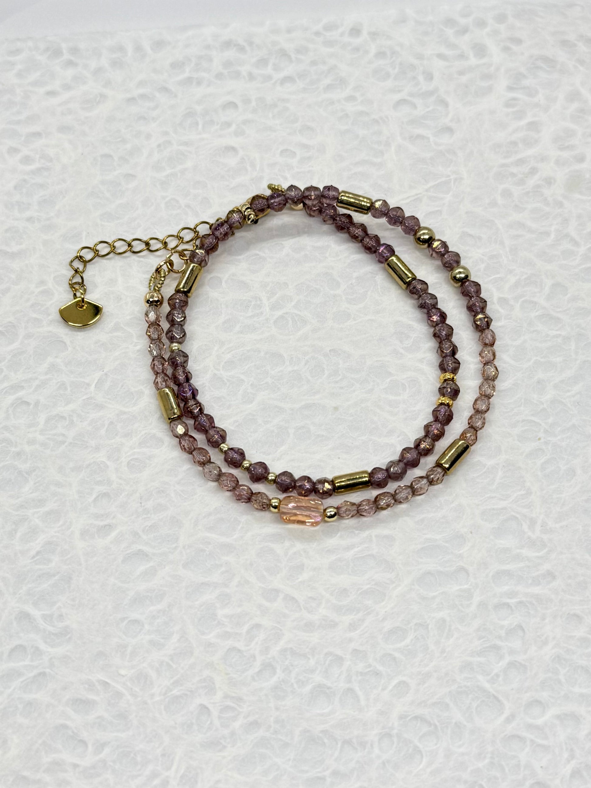 Stack of beaded bracelets with gold accents on a textured white background