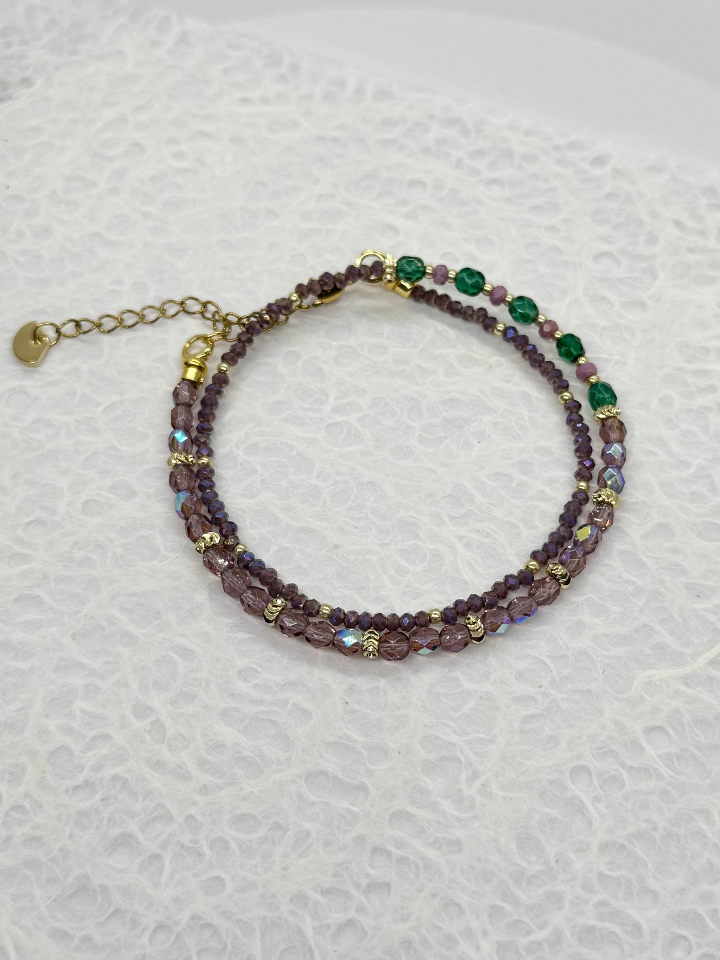 Beaded bracelet with purple and green beads on a textured white background