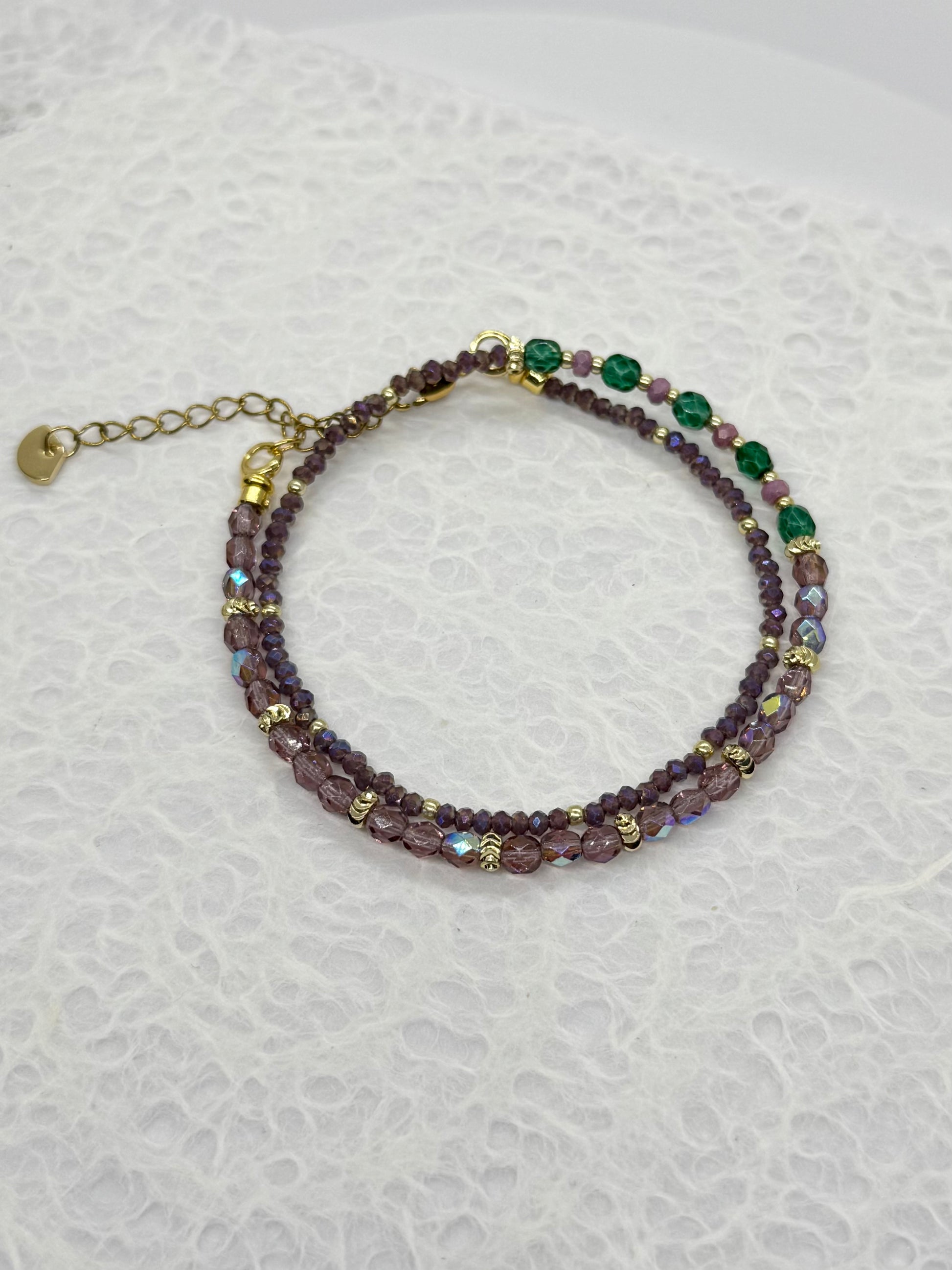 Beaded bracelet with purple and green beads on a textured white background