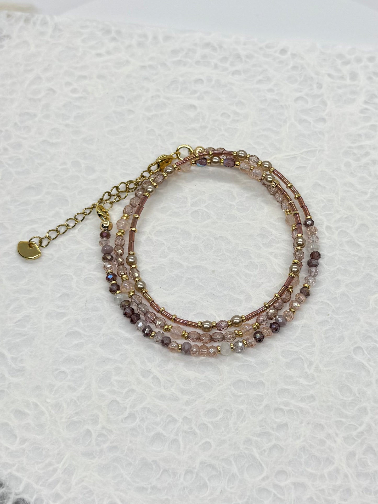 Multistrand beaded bracelet with gold chain on a textured white background