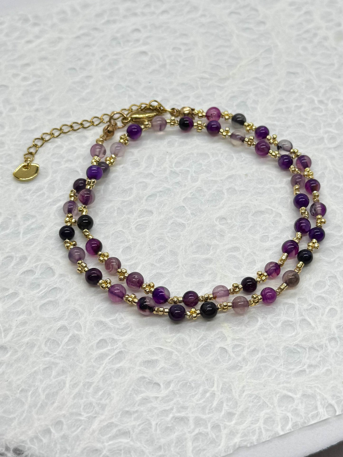 Two-layered beaded bracelet with purple and gold beads on a white background