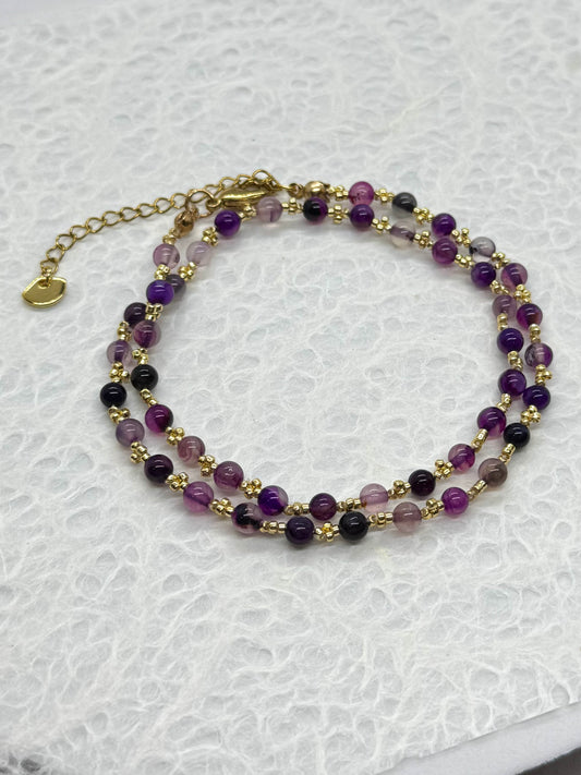 Two-layered beaded bracelet with purple and gold beads on a white background
