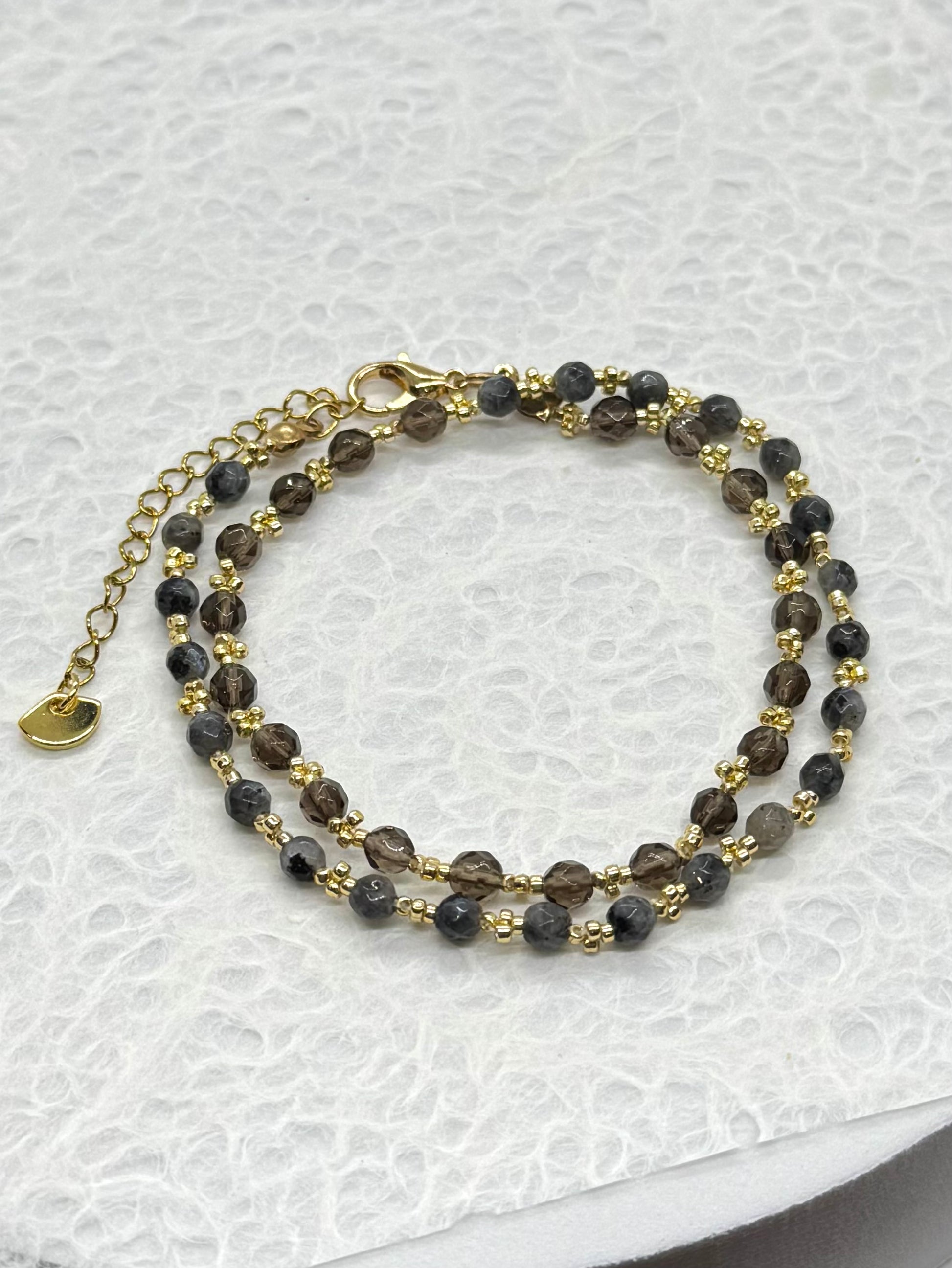 Double-layered beaded bracelet with gold accents on a textured white surface