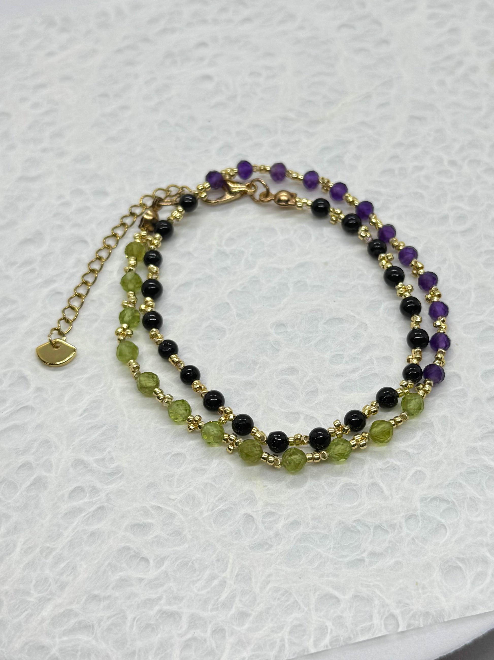 Multistrand beaded bracelet with green, black, and purple beads on a white background