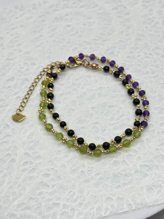 Multistrand beaded bracelet with green, black, and purple beads on a white background