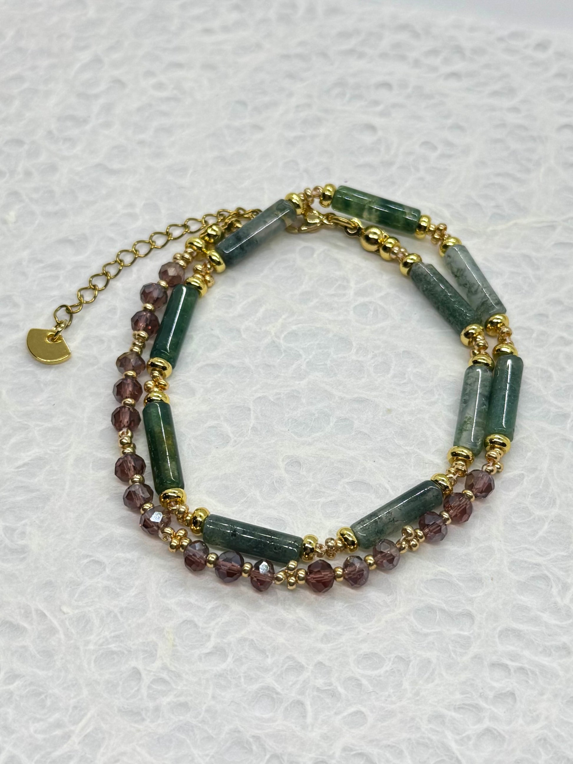 Multistrand bracelet with green and purple beads on a textured white background