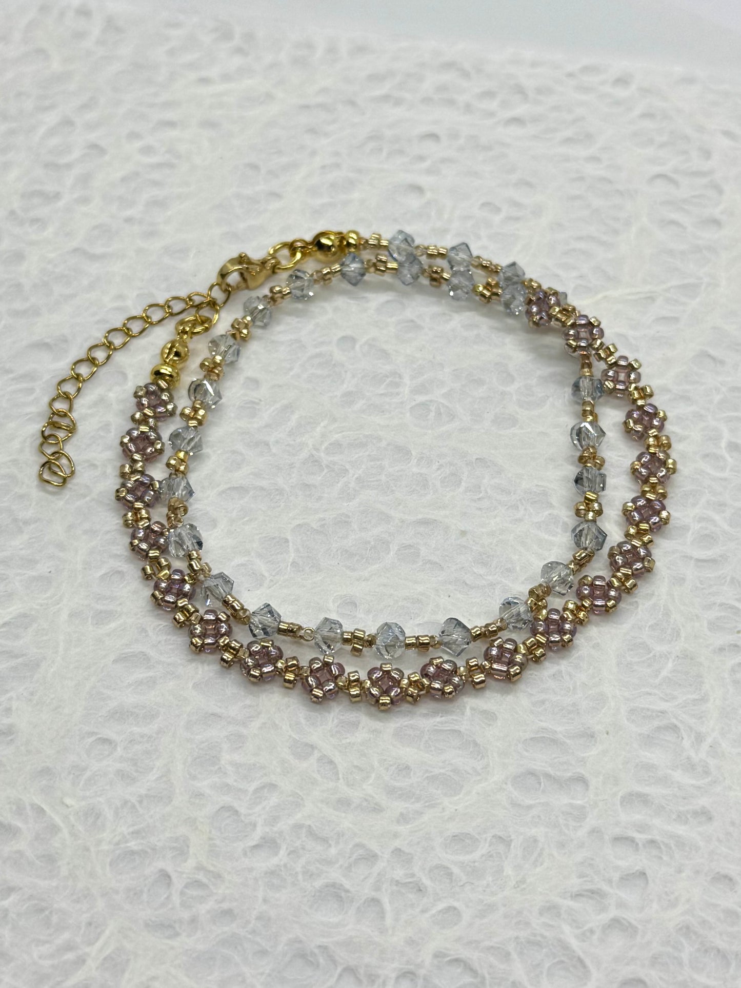 Two-layered beaded bracelet with gold chain on a textured white background