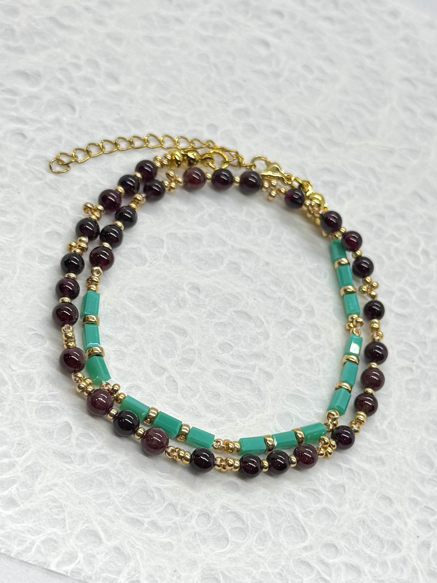 Multistrand beaded necklace with gold chain on a textured white background