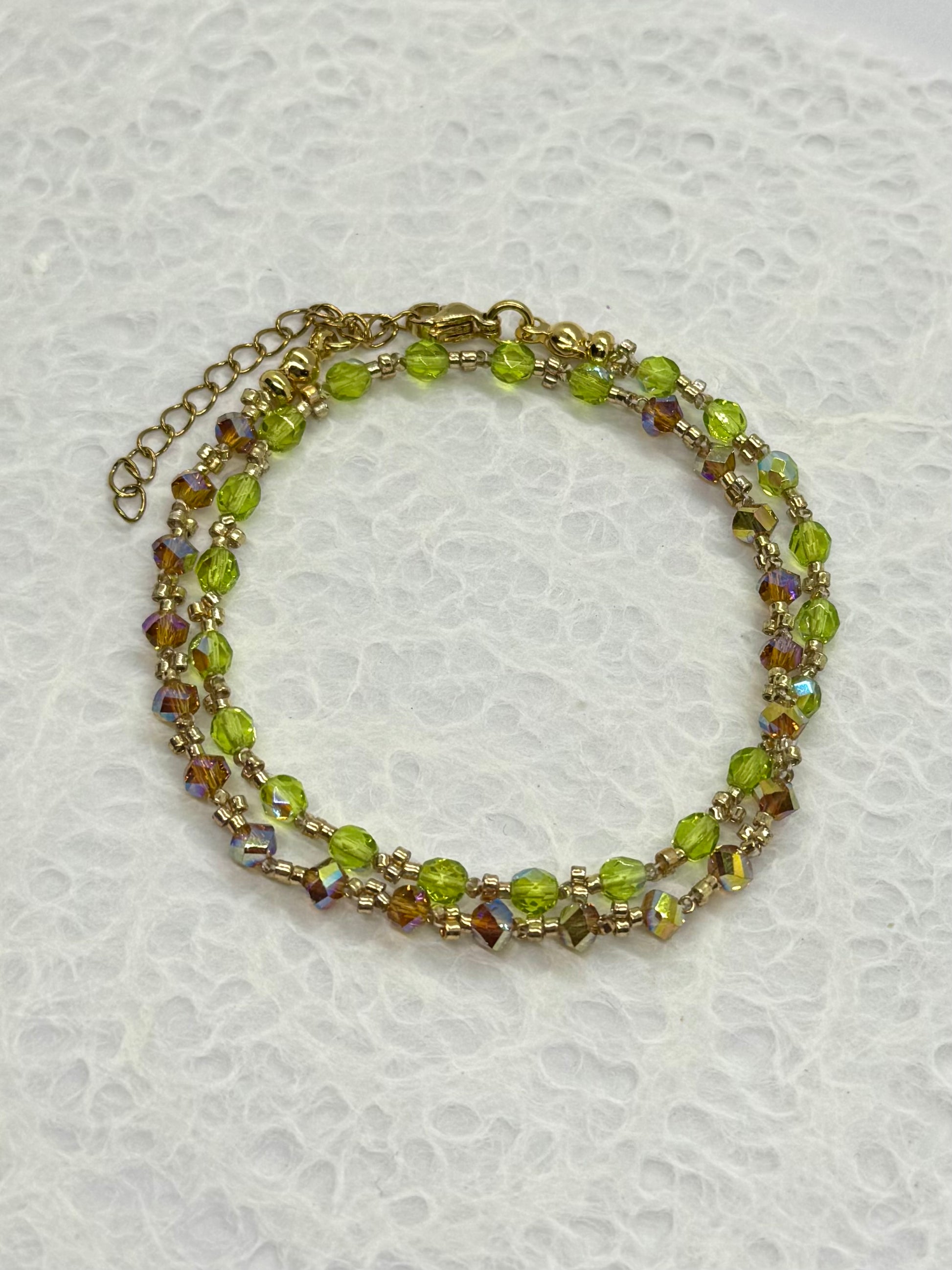 Beaded bracelet with green and gold beads on a textured white background