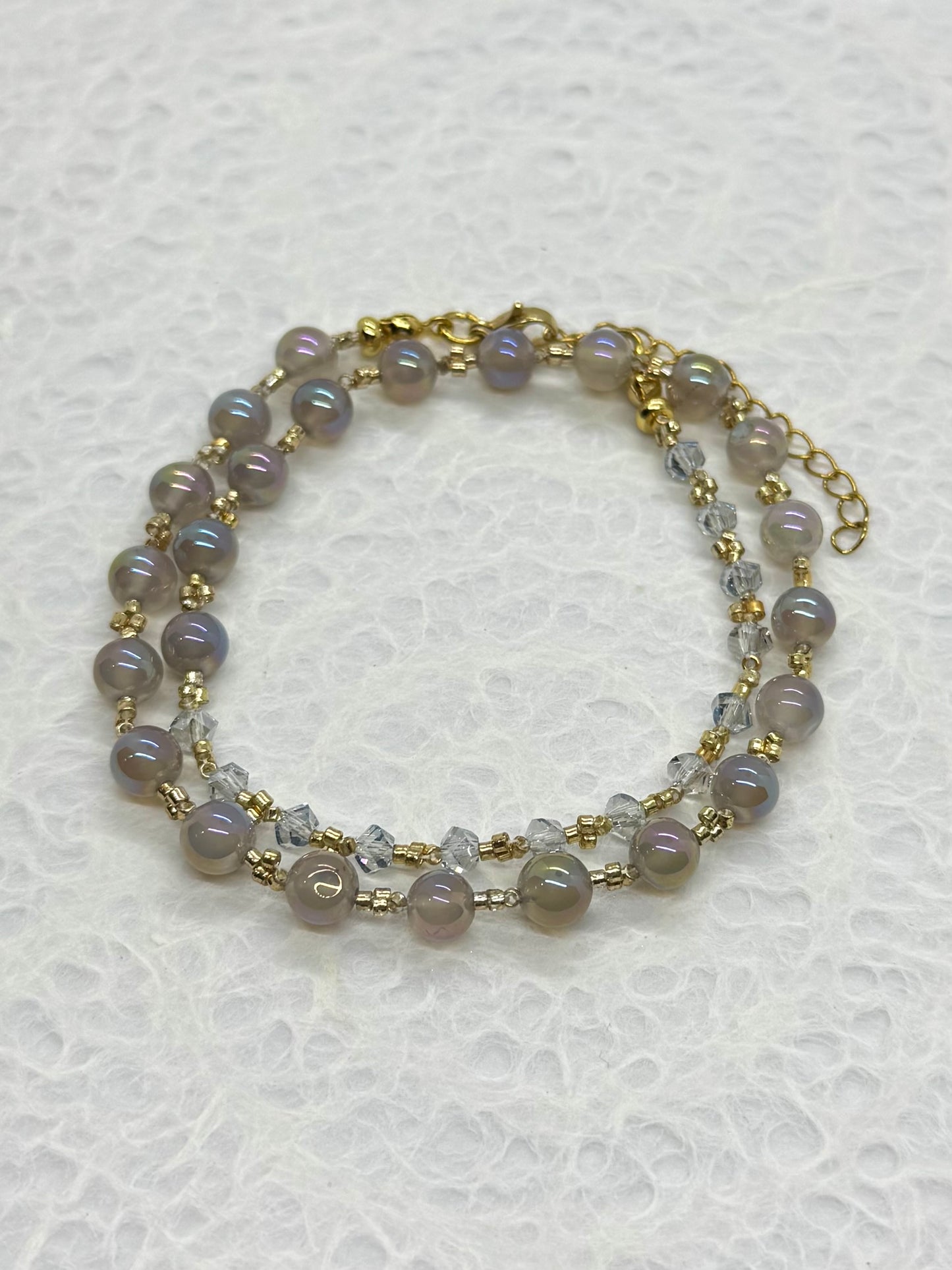Two-layered beaded bracelet with gold accents on a textured white background