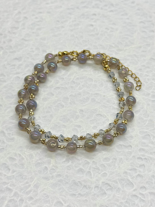 Two-layered beaded bracelet with gold accents on a textured white background