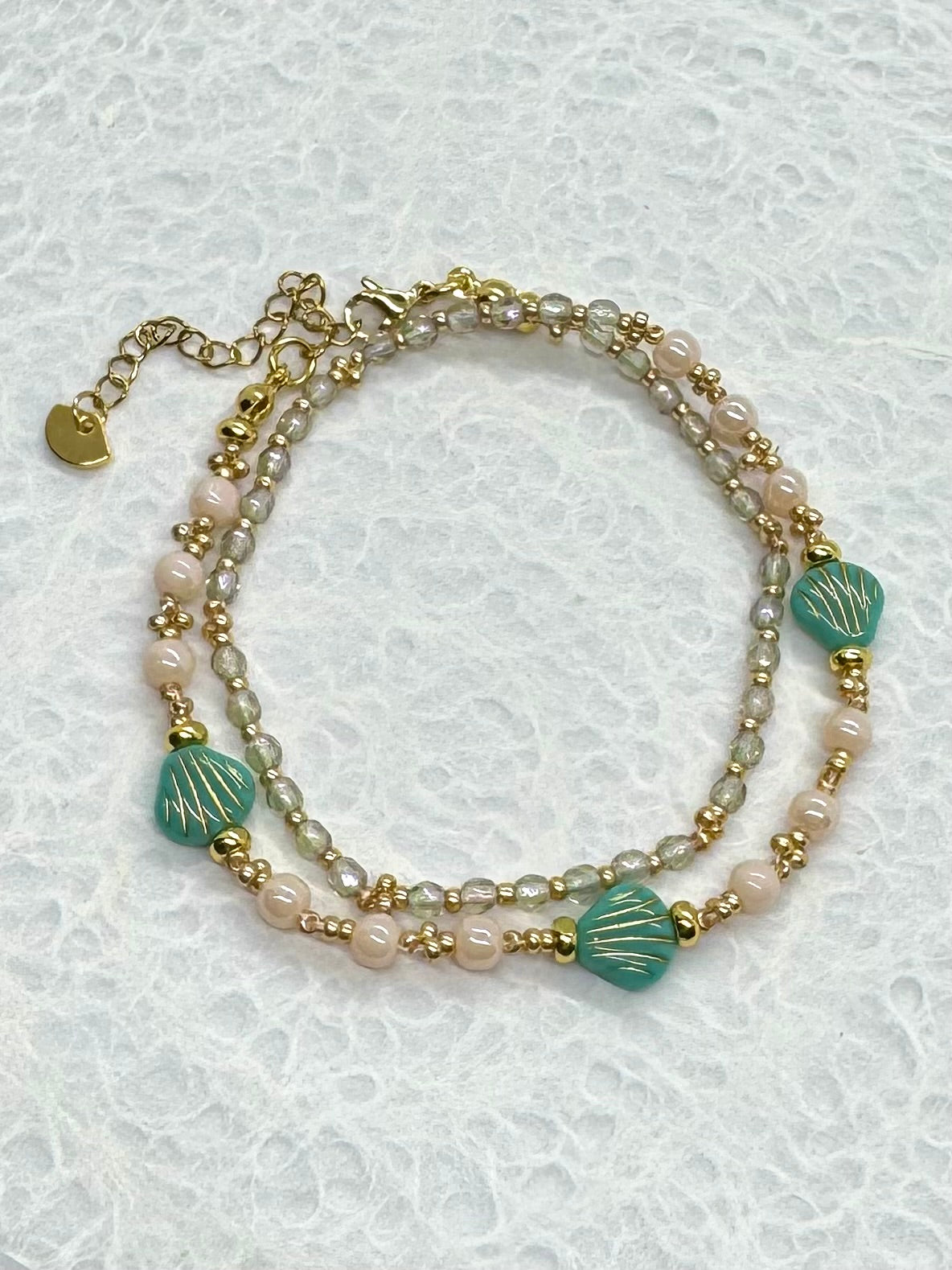 Stack of beaded bracelets with gold accents on a textured white background