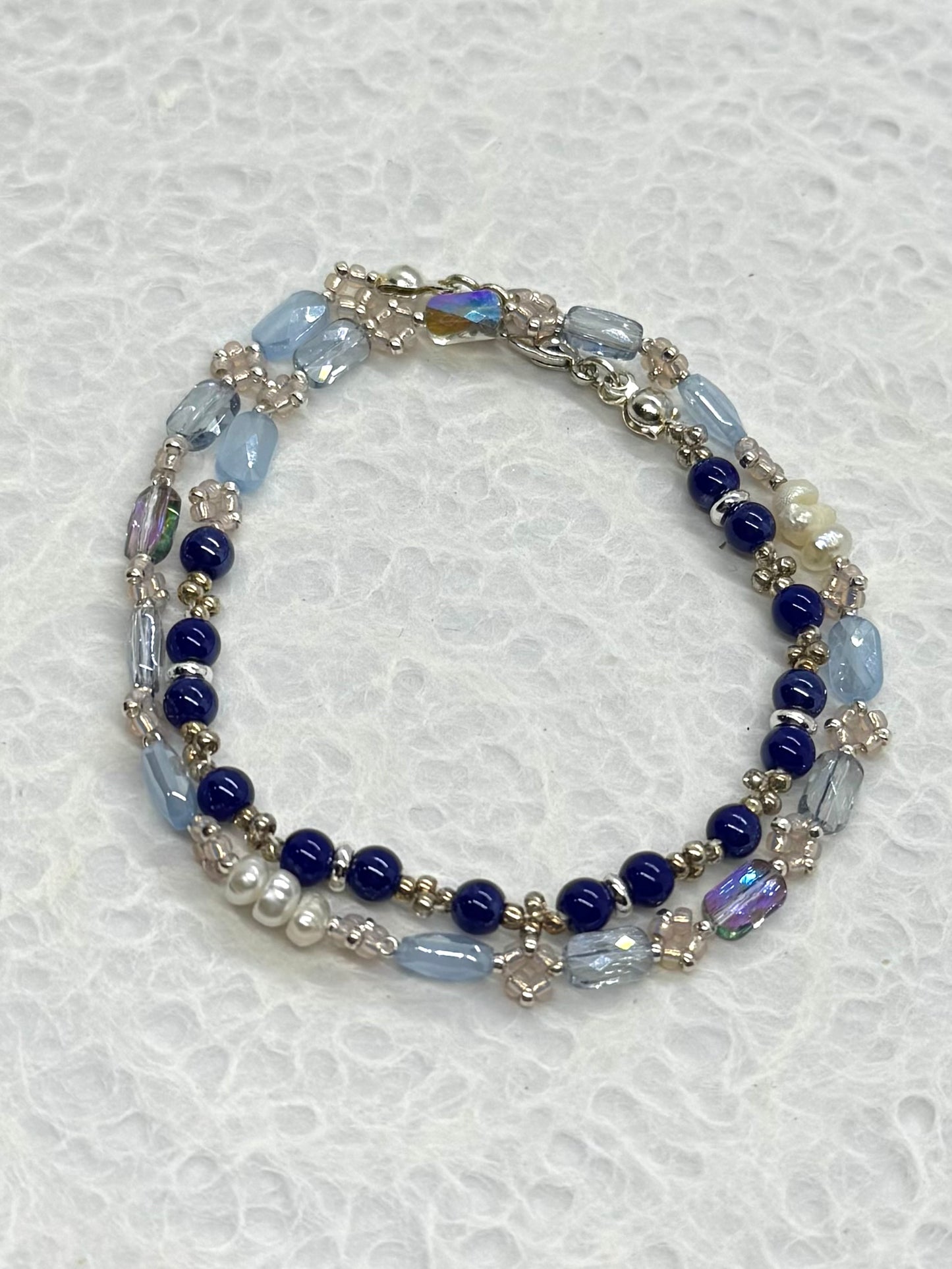 Multistrand beaded bracelet with blue, white, and silver beads on a textured white background