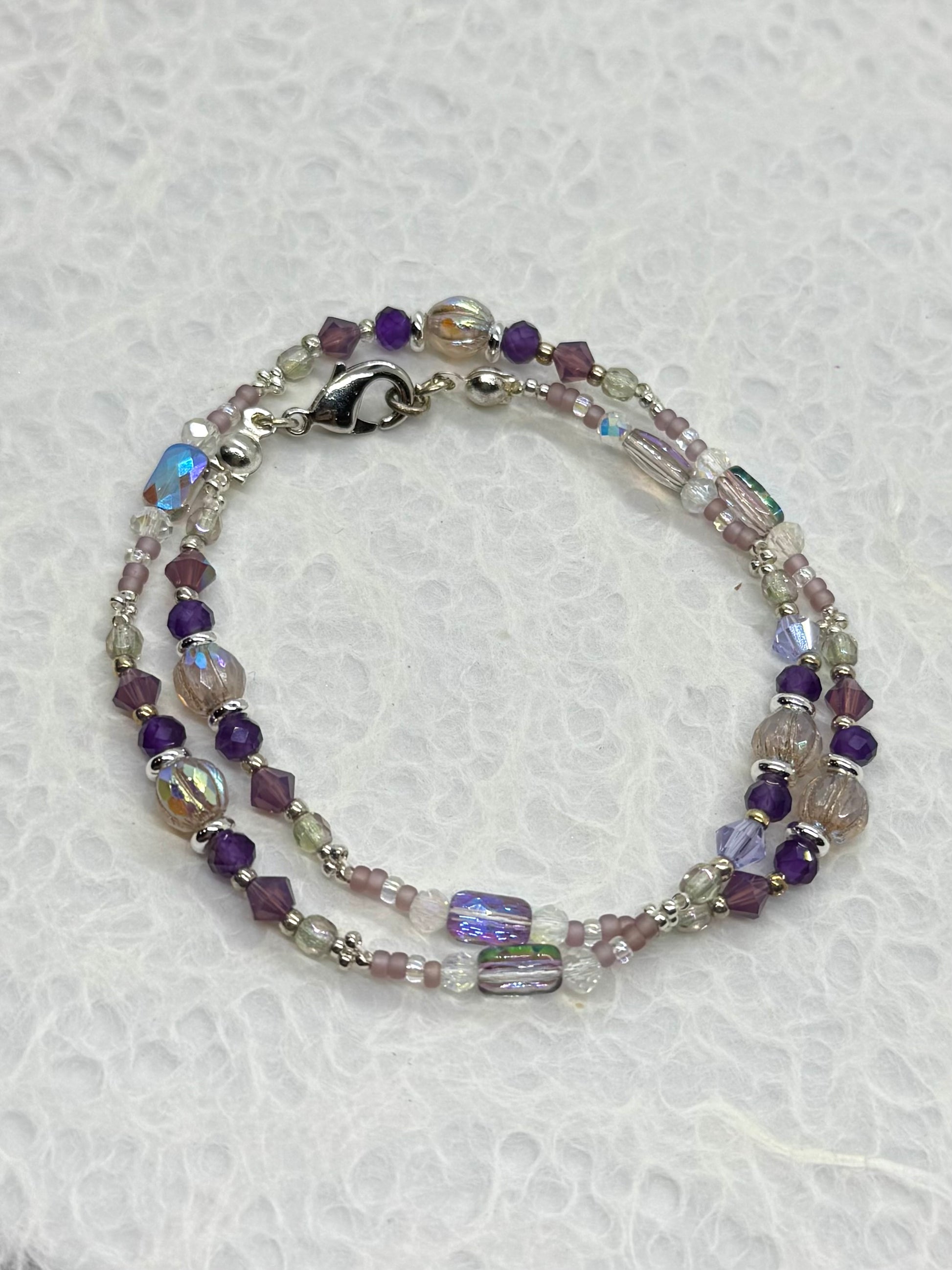 Beaded bracelet with purple and clear beads on a textured white background