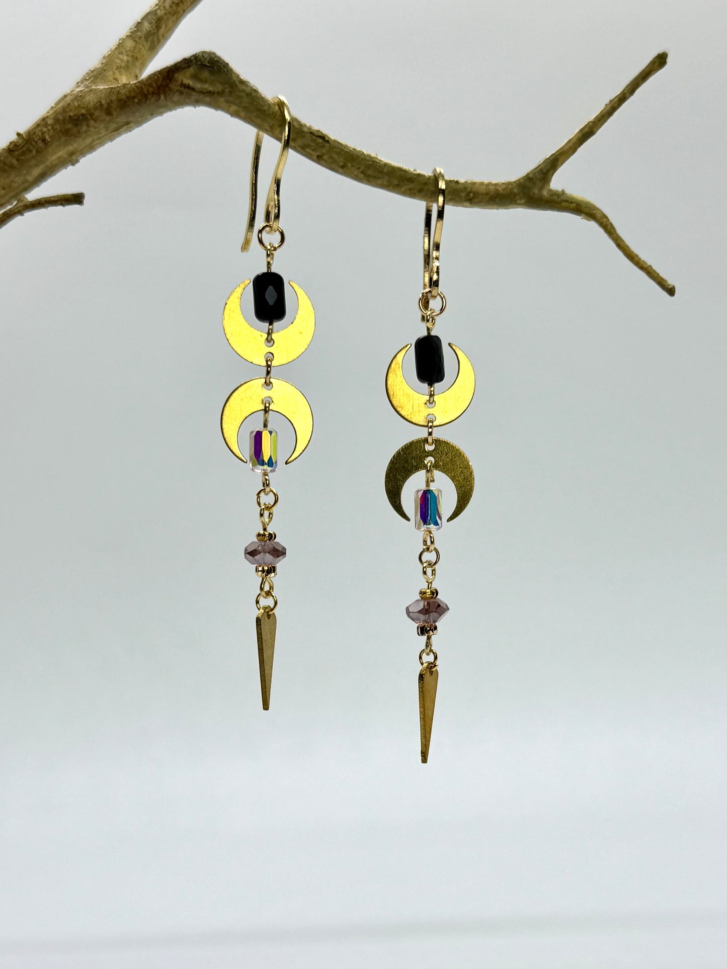 Earrings with gold crescent moon designs and black stones hanging from a branch.