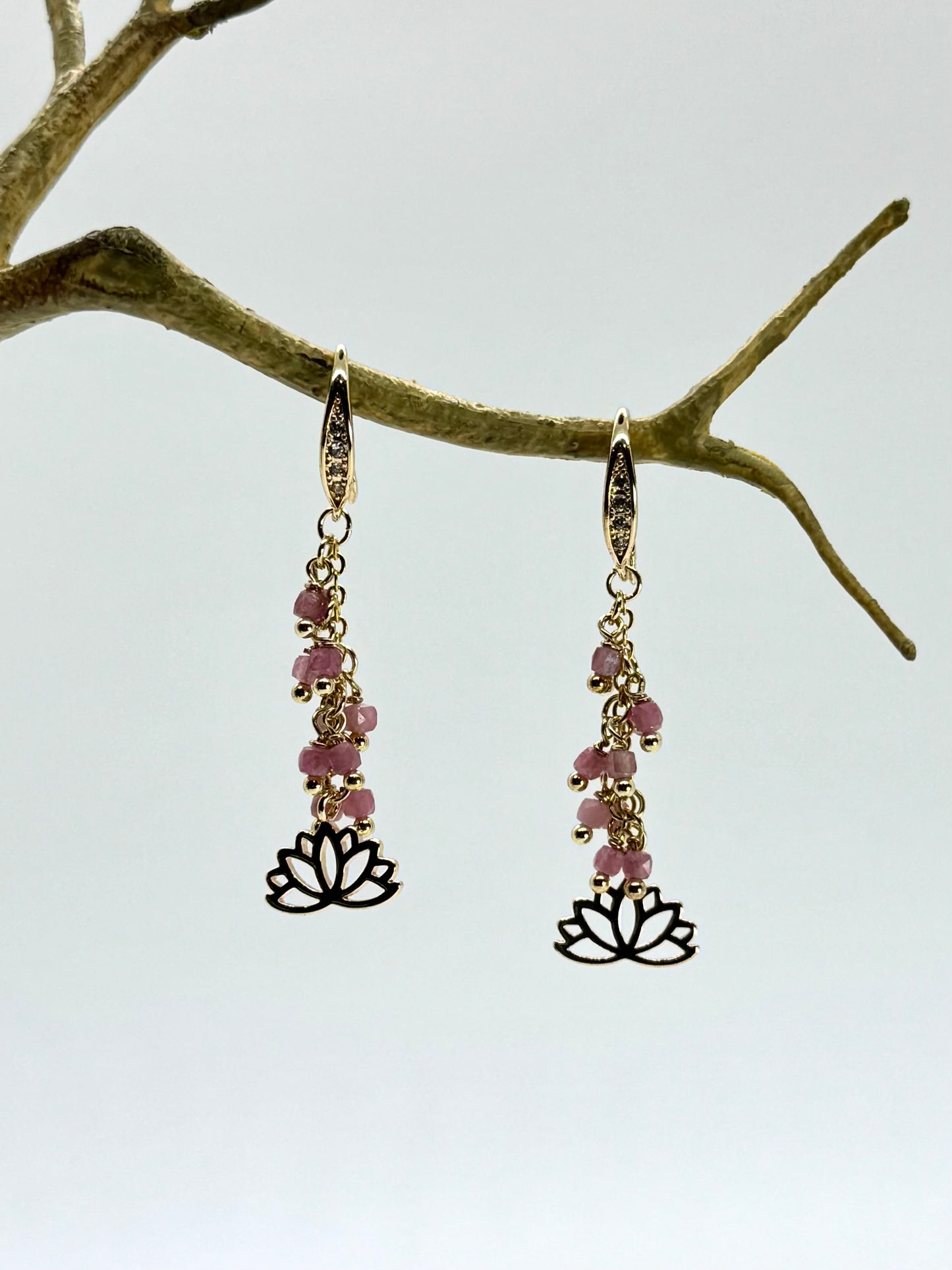 Pair of earrings with pink beads and lotus flower charms hanging from a branch.