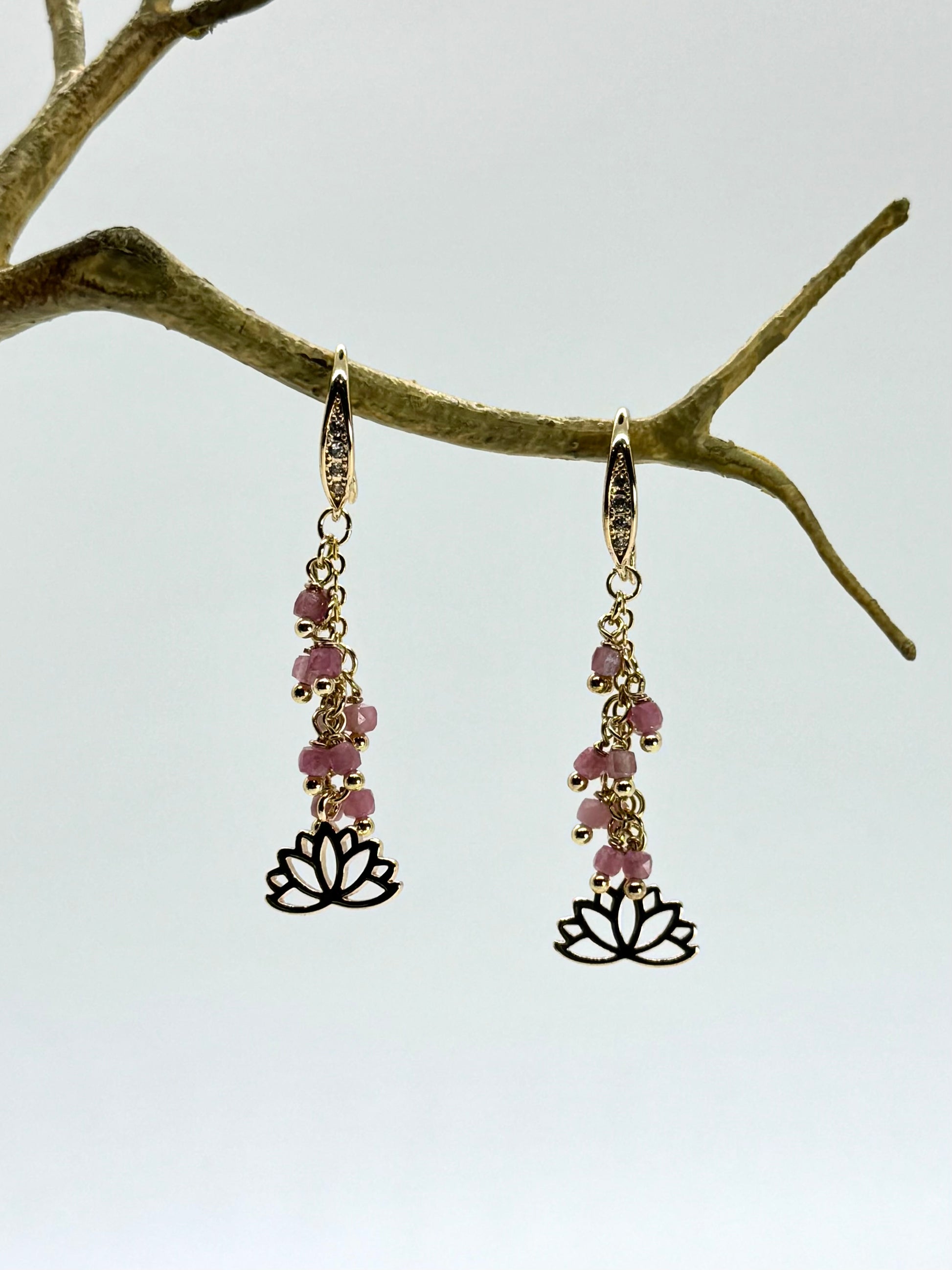 Pair of earrings with pink beads and lotus flower charms hanging from a branch.